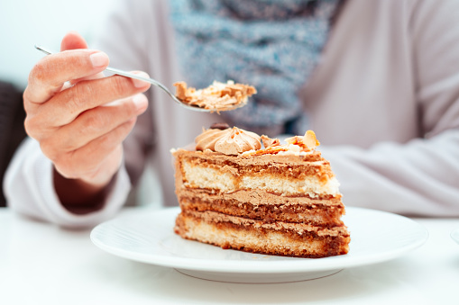 Woman sitting at the cafe table with a slice of coffee cake. Elderly woman ignoring the diet, committing a sin of gluttony