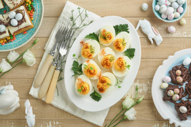 istock Easter stuffed eggs. Traditional Easter brunch or dinner with stuffed eggs with paprika, carrot cake bars and chocolate nest cakes with glazed eggs. Easter meal dishes with holday decorations Top view 1837795927