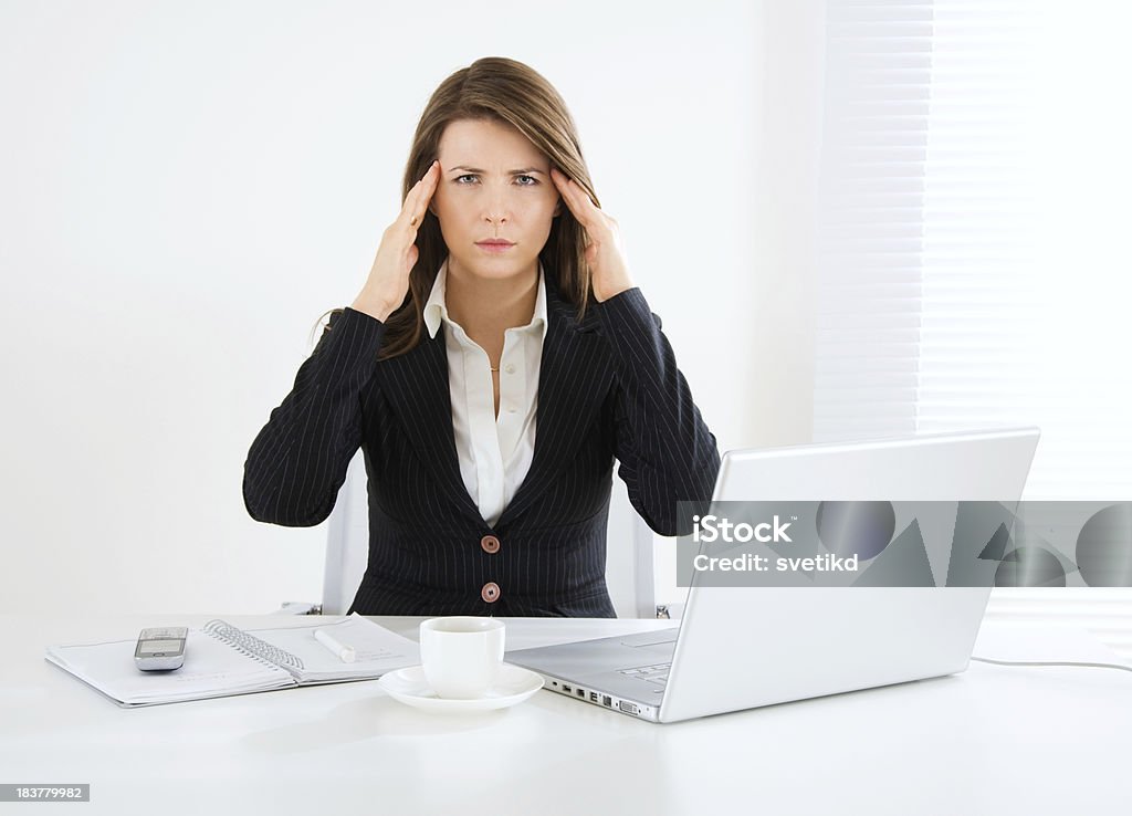 Concentration. Tired businesswoman sitting at her desk in the office and holding hands on her temples. Looking at camera. 30-39 Years Stock Photo
