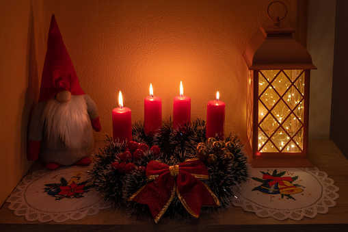 Advent wreath with evergreen boughs and red berries with three candles lit shot from tabletop with copy space