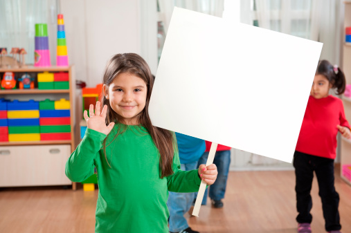 Happy little girl is holding blank placard in the classroom.