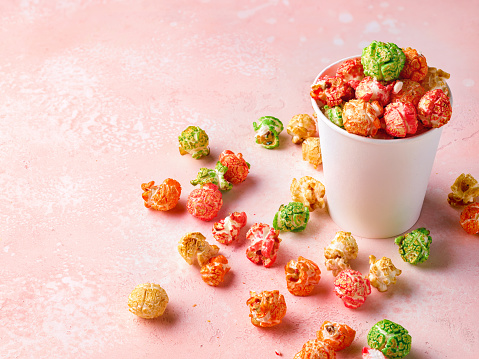 Paper cup of colorful sweet popcorn on pink background. Caramel and fruit flavor