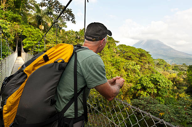 Man hiking in jungle, hanging bridge, Arenal Volcano, Costa Rica Man admiring the beautiful active Arenal Volcano in Costa Rica from an hanging bridge in the jungle. canopy tour photos stock pictures, royalty-free photos & images