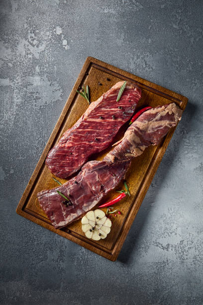 A vertical overhead shot captures the diaphragm steak's marbling. This beef, an alternative cut, sits atop a wooden board, paired with a gray background