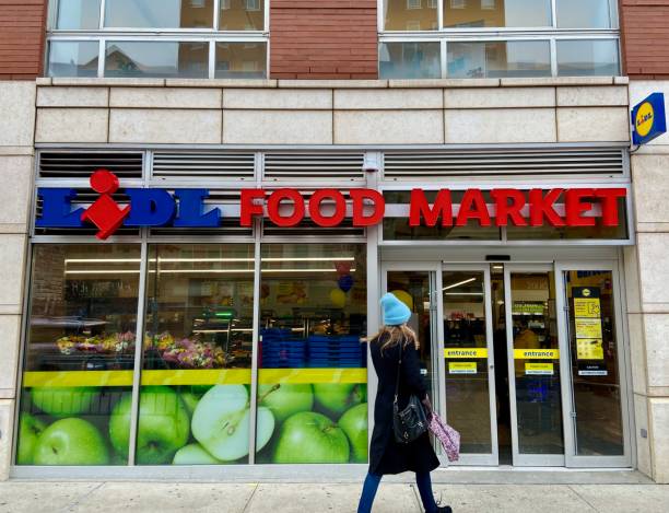 Woman walking into the Lidl grocery store in Harlem, NYC New York, NY USA - February 24, 2022 : A woman walking into the Lidl grocery store on Frederick Douglass Boulevard in Harlem, New York City walking into glass door stock pictures, royalty-free photos & images