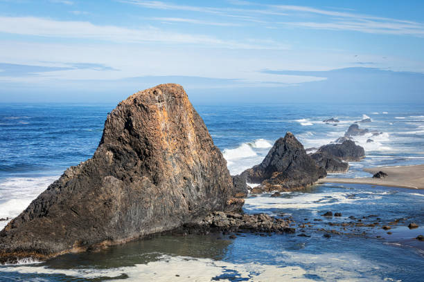 An aerial view from behind the three arch rocks on the Oregon coast with foam on the ocean water surface