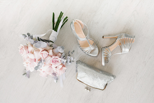 Wedding accessories for the bride: a bouquet of pink roses, bags and shoes on the background