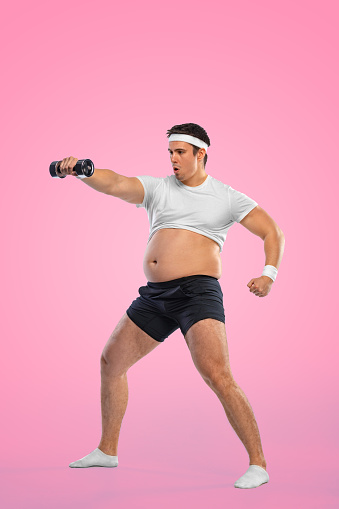 A funny fat man with dubbell isolated on pink background. Obesity and eating disorder. Concept for dietetics and fitness advertising in social networks.