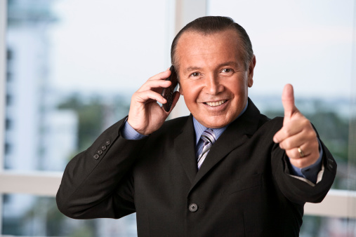 Mature Hispanic smiling businessman talking on phone and gesturing a thumbs up