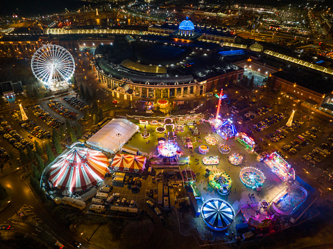 An aerial photograph of a Christmas Fairground at The Trafford Centre in Manchester, England. The photograph shows many of the fairground rides and the dome of the Trafford Centre, illuminated by rich colours.