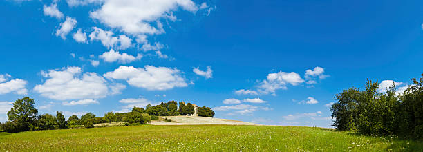 Summer skies over green meadow hilltop country church panorama France Picturesque country church on top of a hill overlooking idyllic Champagne countryside of meadows and pasture in this panoramic vista across rural northern France. ProPhoto RGB profile for maximum color fidelity and gamut. france village blue sky stock pictures, royalty-free photos & images