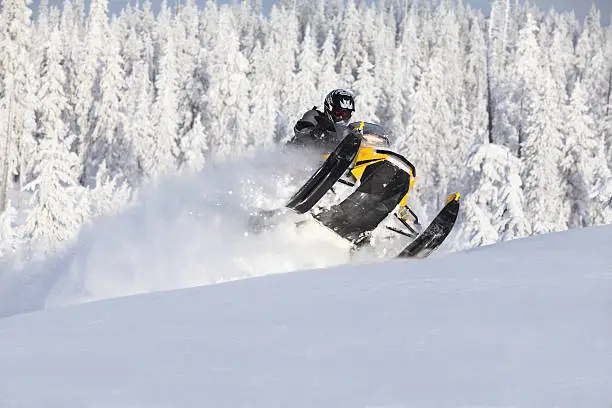 Snowmobiler busting through a drift and jumping