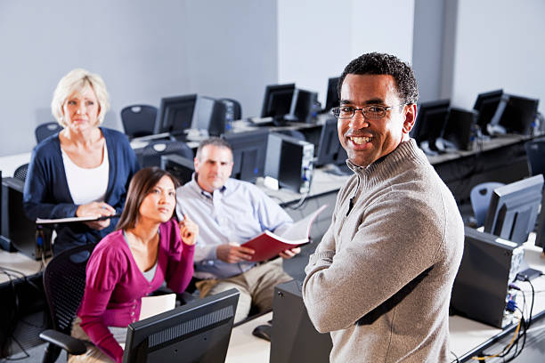 Adult students with instructor in computer lab Continuing education students with teacher.  Focus on African American man standing professor business classroom computer stock pictures, royalty-free photos & images