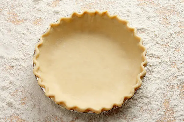 An empty pie crust on a table laden with flour.
