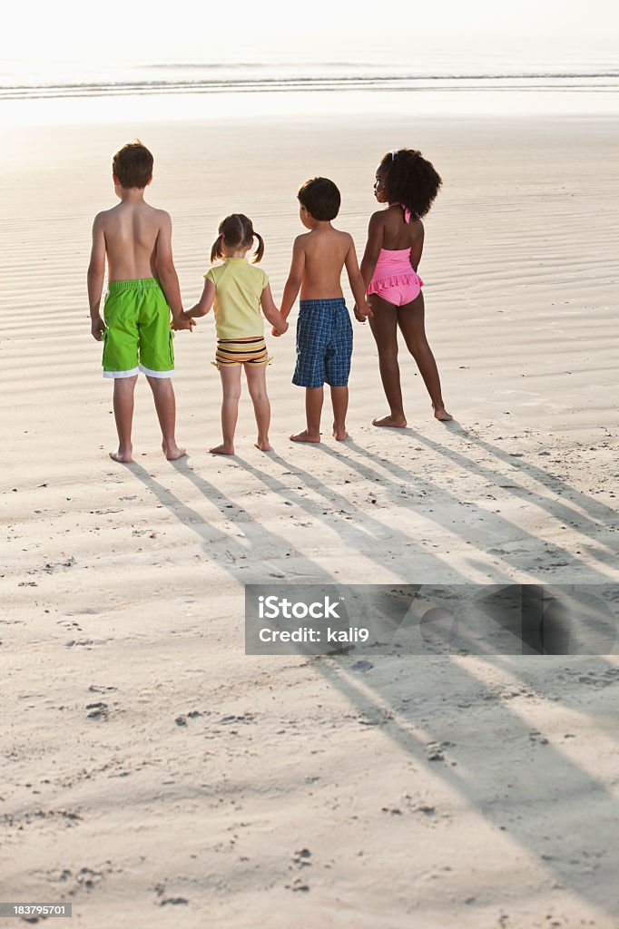 Quatre enfants multiraciales tenant les mains sur la plage - Photo de Enfant libre de droits