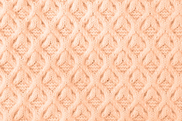 Demonstrating the colors of 2024 - peach color. Knitted peach background. Large knitted fabric with a pattern. Close-up of a knitted blanket.