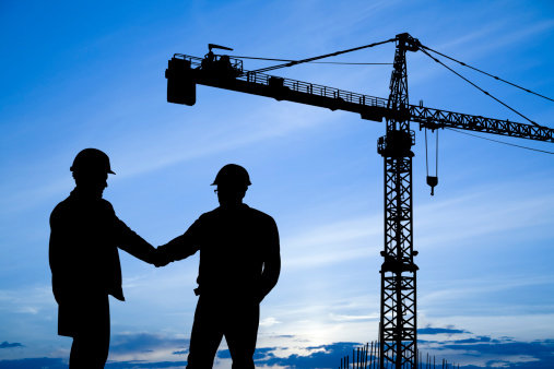 Royalty Free Image of two silhouetted construction workers with a crane in the distance.