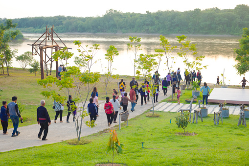 Many thai people tourists at Mekong river catured in late afternoon in Chiang Khong area in Chiang Rai province in north Thailand.. People are walking downt a pathway from small hillside waterfront. At waterfront a local Nakhon shrine is seated. In background is border and land of Laos at Mekong river
