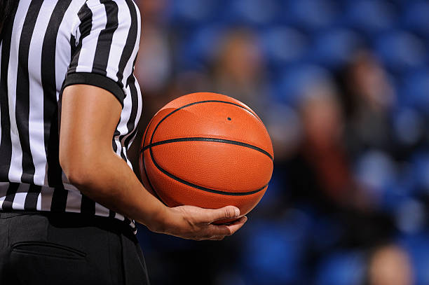 Faceless female basketball referee holds ball in one hand A basketball referee holds a ball during a game. referee stock pictures, royalty-free photos & images