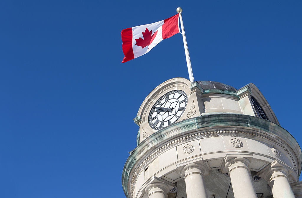 The clock tower in Kitchener's Victoria Park with the Canadian Flag against a brilliant blue sky.