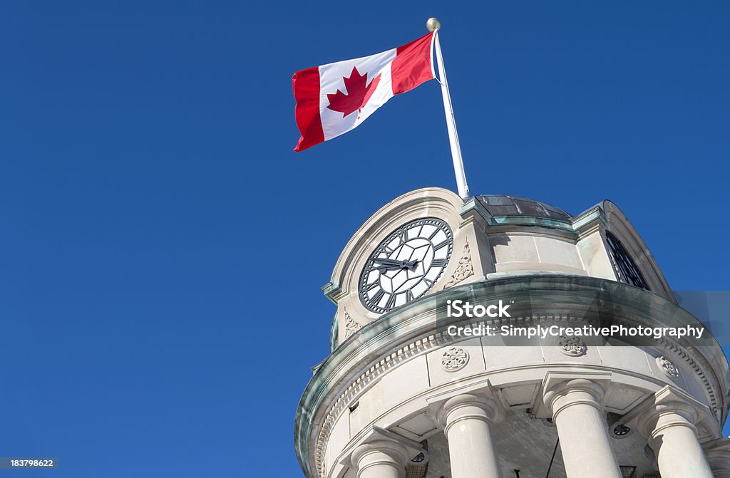 Low angle view of a Canadian flag flying on a clock tower The clock tower in Kitchener's Victoria Park with the Canadian Flag against a brilliant blue sky. Victoria Day - Canada Stock Photo