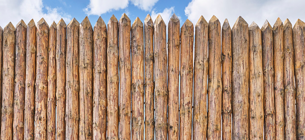 Palisade and a little of cloudy sky as abstract rustic or historical background. Fence made of tightly driven stakes. Banner. Copy space