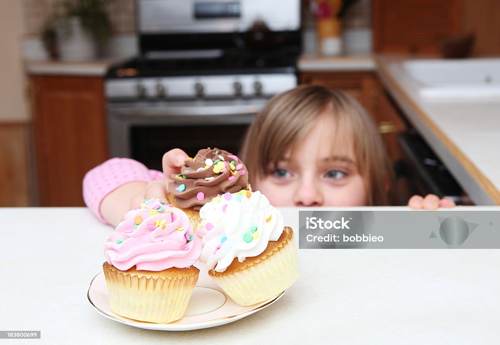 Little girl sneaking cupcake Little girl peeking over the counter while sneaking a cup cake Child Stock Photo