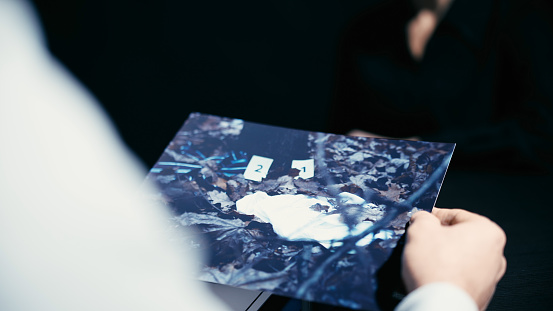 A male detective is studying a photo from the crime scene and asking questions to a suspect person