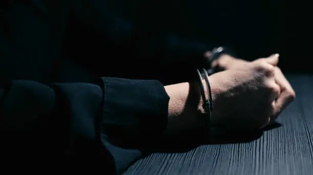 Female hands in handcuffs are leaning on a table in an interrogation room, close-up