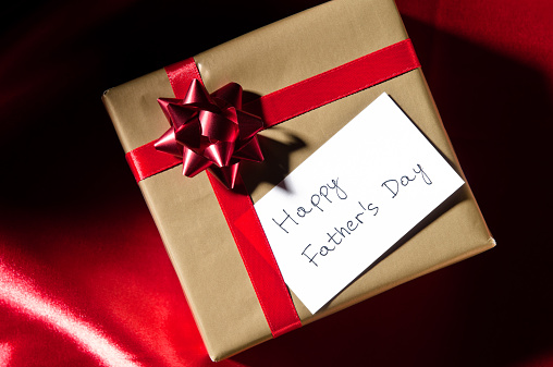 Happy Father's Day, gift with red ribbon against red background.