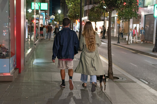 Gijón, Spain. 10/18/2023. Young couple walking through the city at night with their dog