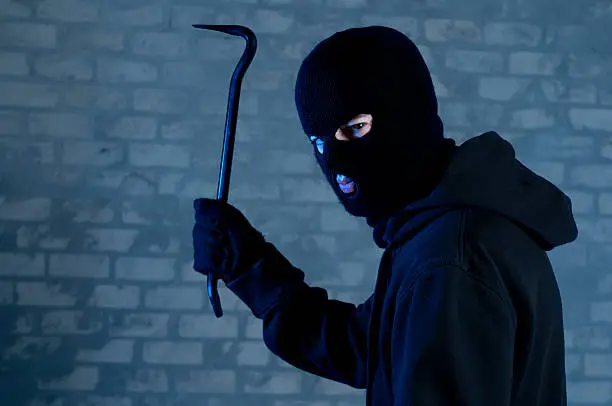 Criminal disguised with balaclava raises a crowbar above his head: ready to attack or trespass.