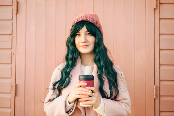Stylish young smiling hipster woman with color hair wearing trendy peach color coat and hat with reusable coffee cup on wooden background. Urban seasonal city street fashion. Color of the 2024 year. Stylish young smiling hipster woman with color hair wearing trendy peach color coat and hat with reusable coffee cup on wooden background. Urban seasonal city street fashion. Color of the 2024 year 2024 30 stock pictures, royalty-free photos & images