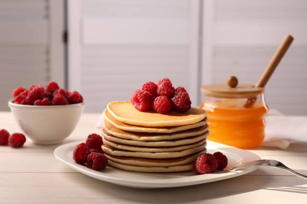 istock Stack of tasty pancakes with raspberries and fork on white wooden table 1838041248