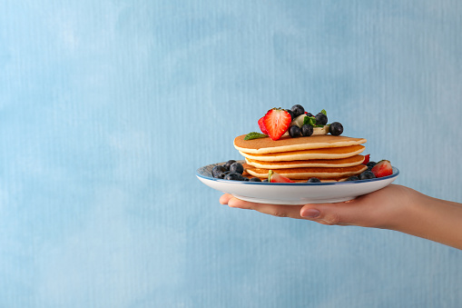 Woman holding delicious pancakes with fresh berries and butter against light blue background, closeup. Space for text