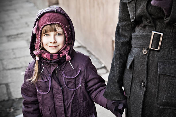 Smiling little girl holding hands with mother on damaged pavement.