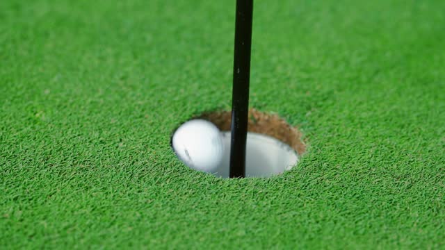 A close-up of a golf ball rolling straight into the hole on the golf course.