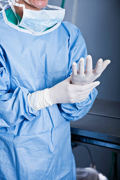 medizinische arbeiter putting auf latex-handschuhe - operationskittel stock-fotos und bilder