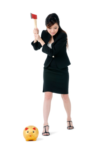 Portrait of a beautiful businesswoman about to break the piggy bank with an axe, over white background.