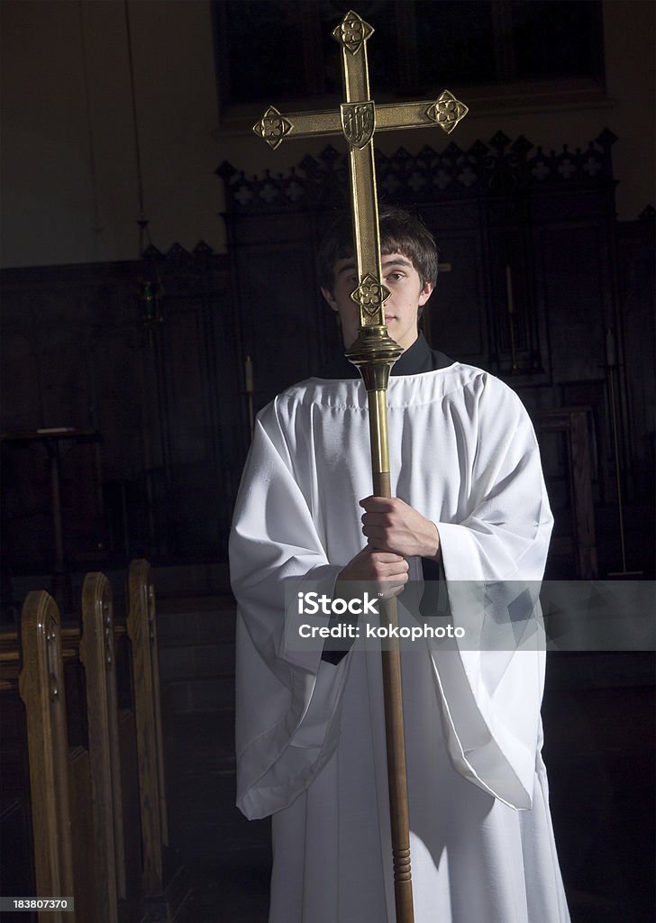 Alcolite Holding Cross in Darkened Church Alcolite holding cross in aisle between church pews in darkened church. Altar Boy Stock Photo