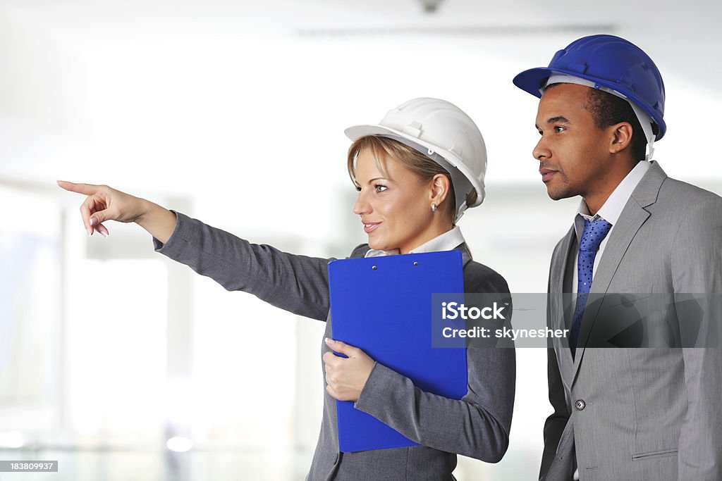 Jóvenes arquitectos trabajando juntos, mujer mostrando con el dedo. - Foto de stock de Accesorio de cabeza libre de derechos