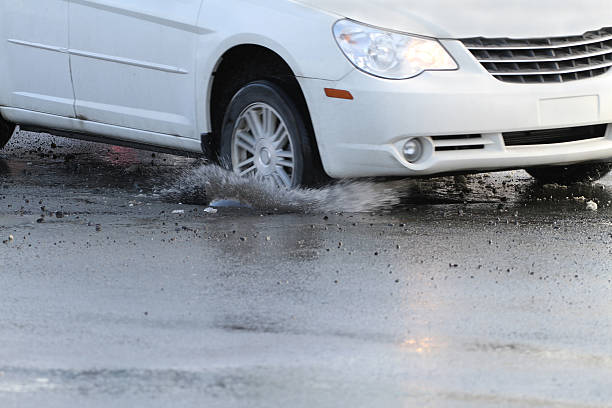 Hitting A Pothole "A car hits a pothole on a city street, throwing up water and debris. Shallow dof with focus only on the pothole and water splash." sinkhole stock pictures, royalty-free photos & images