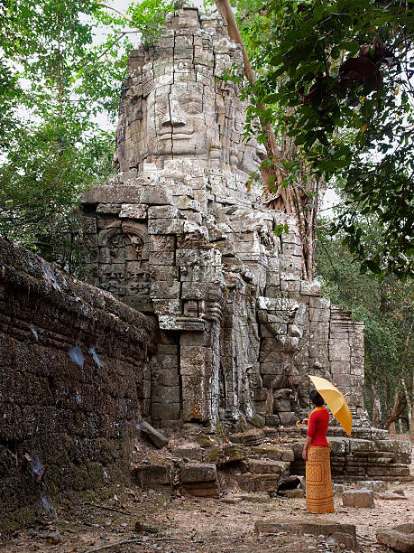 Four-Faced Buddha - Ta Prohm, Siem Reap "Young girl admiring the Four-faced Buddha at the North Gate of Ta Prohm, one of the largest temple and monestary built in the late 12th century of the Khmer civilization.Next to Angkor Wat, Ta Prohm is among the most well known of monuments in Siem Reap, Cambodia.Related files:" khmer stock pictures, royalty-free photos & images