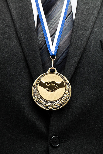 businessman in grey suit with gold medal and handshaking symbol