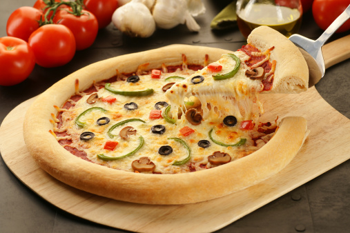Slice of veggie pizza being lifted from a freshly baked whole pie.