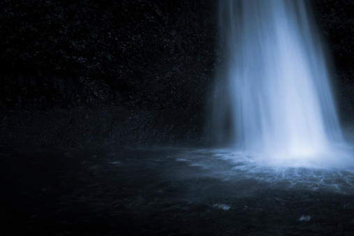 Dreamy image of water falling into a pool of water in low light with plenty of copyspace.