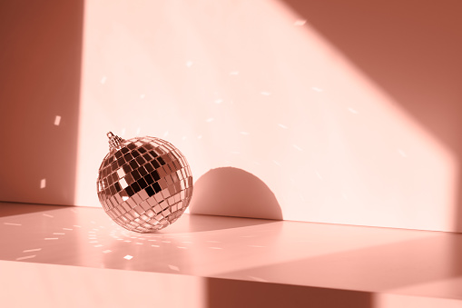 Disco ball in sunlight with reflections on white background. Geometric shadows peach color trend 2024
