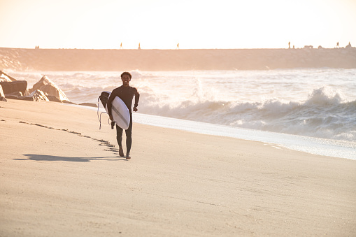 Man surfer run in the beach near the ocean with surfboard.