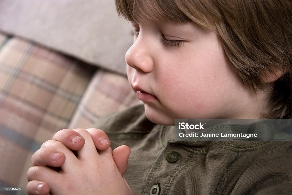 Little Boy Praying A little boy sits with his hands together praying. Blond Hair Stock Photo