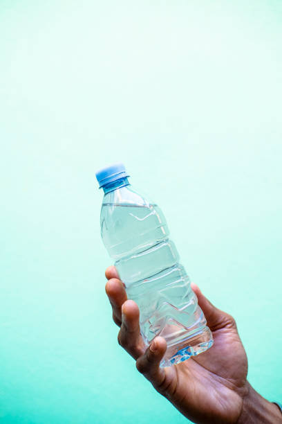 A man's hand is holding a plastic bottle in front of a blue wall.
